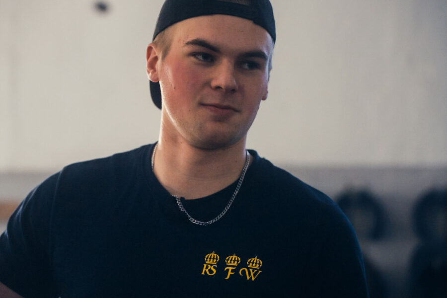Ung man i svart keps och svart tröja med gul logotyp inomhus