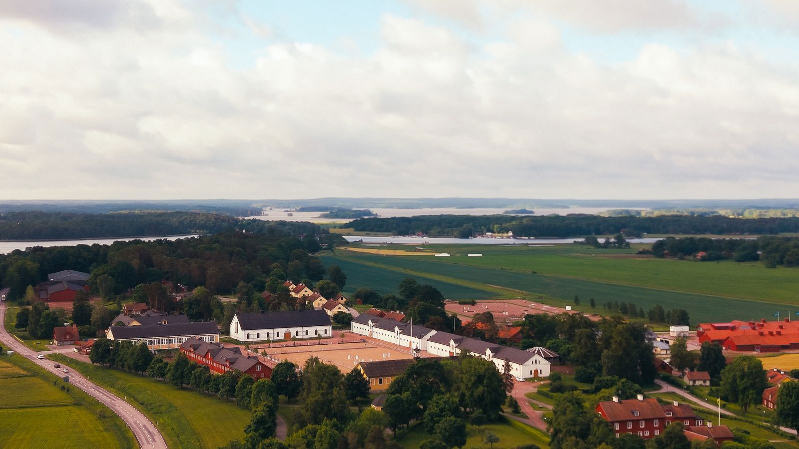 Flygvy över gård med ridhus och omgivande åkrar, skog och sjöar
