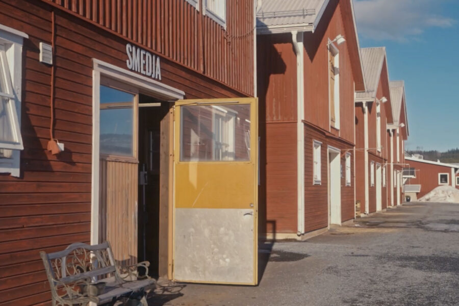 Röd träbyggnad med skylten Smedia och en öppen gul dörr i en rad av industribyggnader